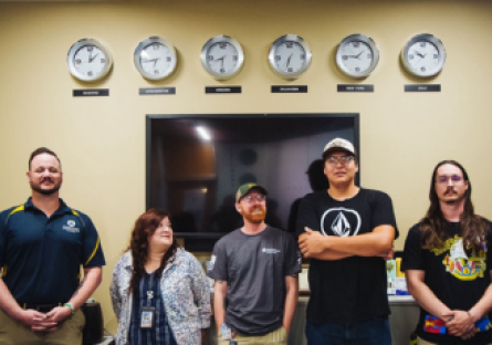 Five veterans gather in Phoenix College's Veteran Services Student Center and stand under six clocks showing the time at various locations around the world. 