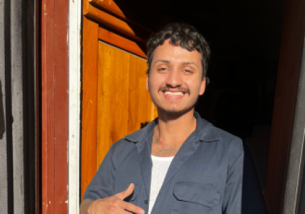 Phoenix College student Luis Duque stand at his front door in a gray jumpsuit and big smile.  He was recently awarded TheDream.US scholarship. 