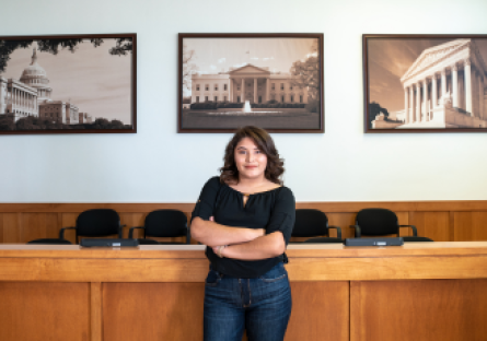 A Phoenix College Paralegal student stands with her arms crossed in front of a courtroom. 